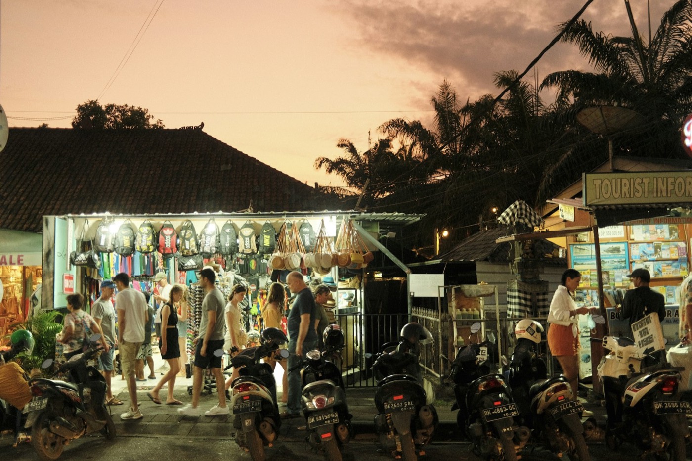 Shoppers and parked scooters outside a lit-up souvenir shop at dusk in Bali